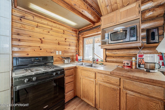 kitchen featuring beam ceiling, sink, black gas range oven, wood walls, and light wood-type flooring