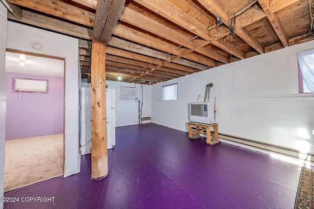 basement with heating unit, white refrigerator, and a baseboard heating unit