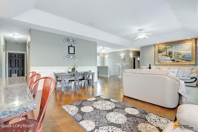 living room with ceiling fan, a tray ceiling, and concrete floors