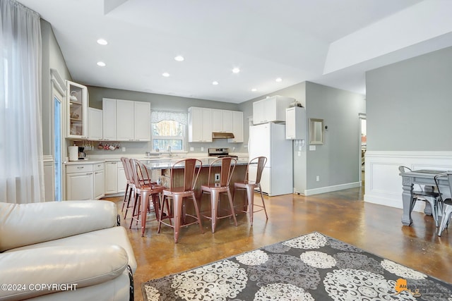 kitchen with a center island, white refrigerator, stainless steel range, a kitchen bar, and white cabinetry