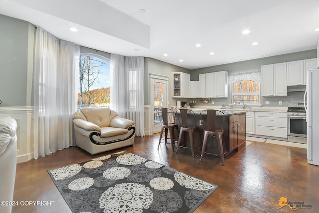 kitchen with a kitchen island, stainless steel range, white fridge, a kitchen bar, and white cabinetry