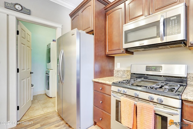 kitchen with light stone countertops, light hardwood / wood-style flooring, crown molding, stacked washer / drying machine, and appliances with stainless steel finishes