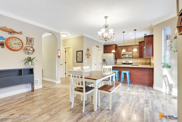 dining room featuring sink, light hardwood / wood-style flooring, ornamental molding, and a notable chandelier