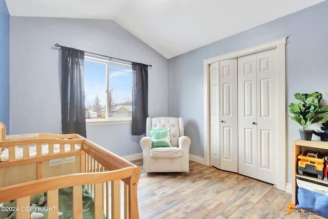 bedroom featuring a closet, light hardwood / wood-style flooring, a nursery area, and lofted ceiling