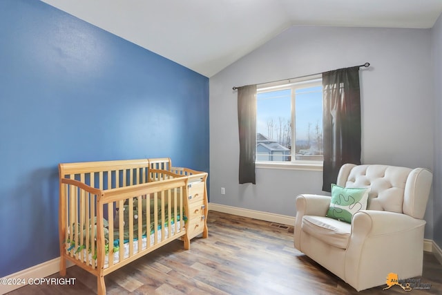 bedroom featuring a crib, hardwood / wood-style flooring, and lofted ceiling