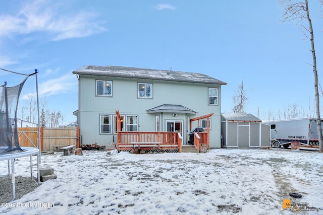 snow covered house featuring a storage unit, a deck, and a trampoline