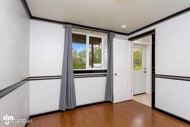 empty room with ornamental molding, plenty of natural light, and light hardwood / wood-style floors