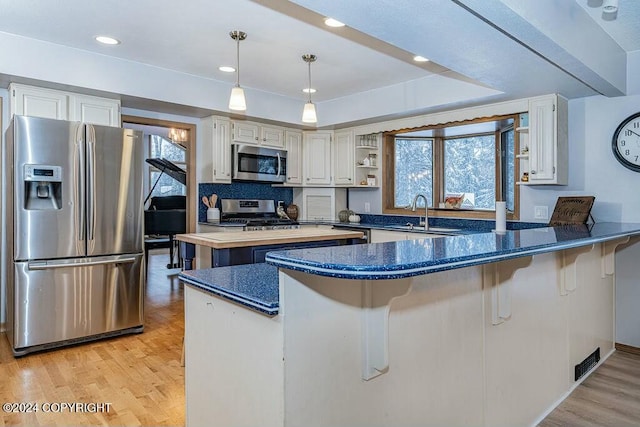 kitchen with kitchen peninsula, stainless steel appliances, sink, white cabinets, and light hardwood / wood-style floors