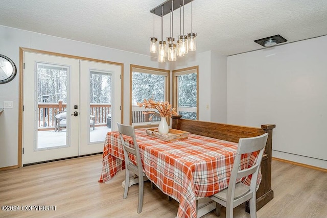 dining area with a textured ceiling, light hardwood / wood-style flooring, and french doors