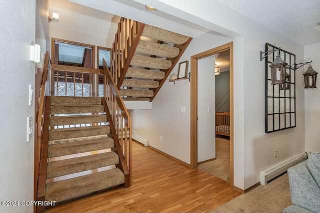 stairs featuring a textured ceiling, wood-type flooring, and baseboard heating