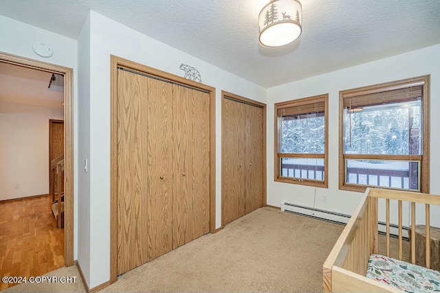 carpeted bedroom with multiple closets, a baseboard radiator, and a textured ceiling