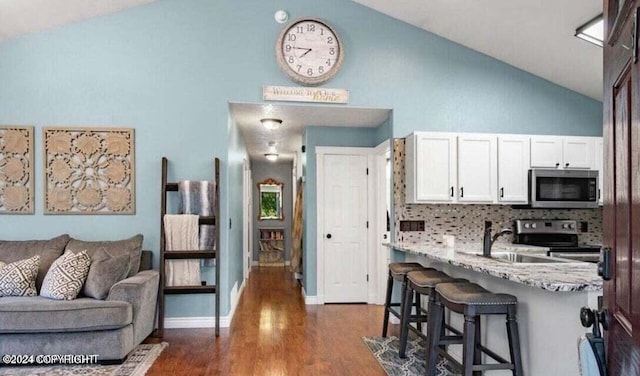 kitchen featuring stainless steel appliances, light stone counters, dark hardwood / wood-style flooring, lofted ceiling, and white cabinets