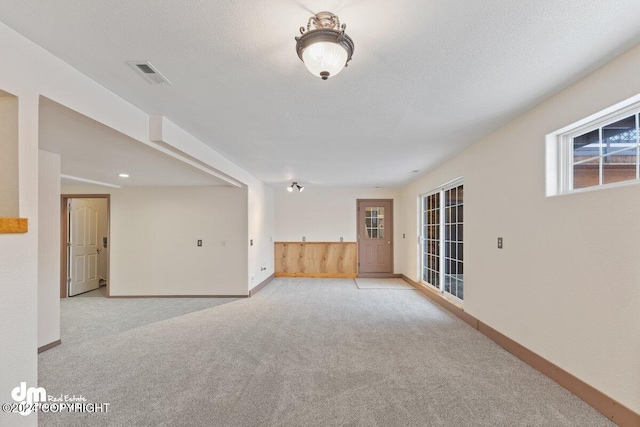 interior space featuring a textured ceiling, light colored carpet, and wooden walls