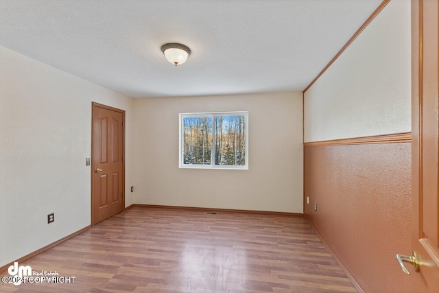 spare room featuring a textured ceiling and light hardwood / wood-style floors