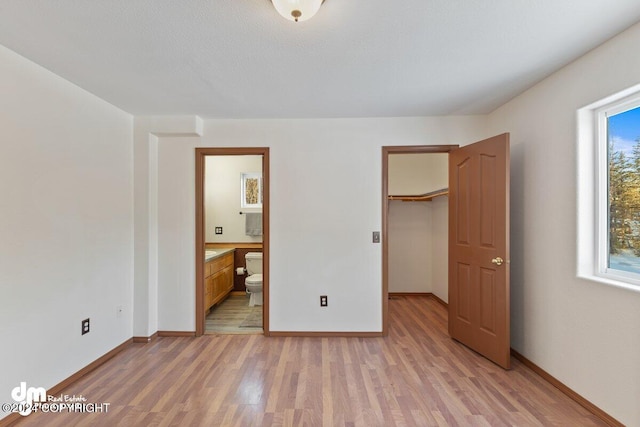 unfurnished bedroom with light hardwood / wood-style floors, a spacious closet, a closet, and ensuite bathroom