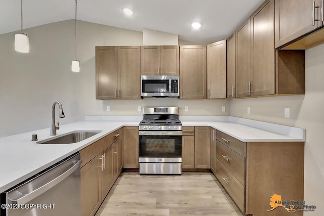 kitchen featuring stainless steel appliances, sink, decorative light fixtures, light hardwood / wood-style flooring, and lofted ceiling