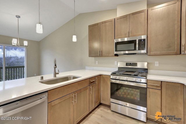 kitchen featuring hanging light fixtures, sink, vaulted ceiling, appliances with stainless steel finishes, and light hardwood / wood-style floors