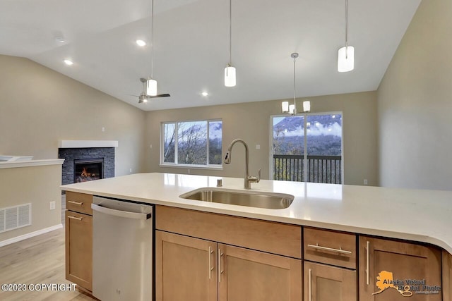 kitchen with a stone fireplace, vaulted ceiling, stainless steel dishwasher, ceiling fan, and light wood-type flooring