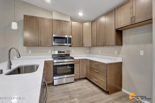 kitchen with lofted ceiling, sink, hanging light fixtures, light hardwood / wood-style flooring, and stainless steel appliances