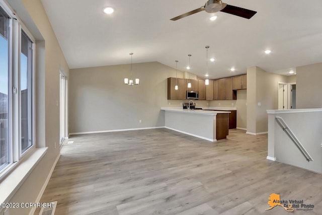 kitchen with sink, kitchen peninsula, light hardwood / wood-style floors, decorative light fixtures, and vaulted ceiling