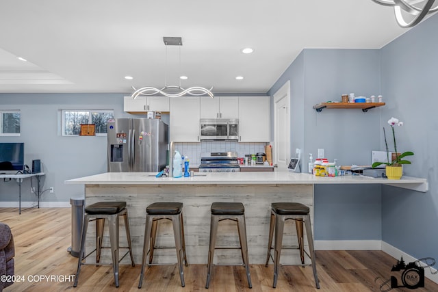 kitchen featuring a kitchen breakfast bar, white cabinetry, light wood-type flooring, and appliances with stainless steel finishes