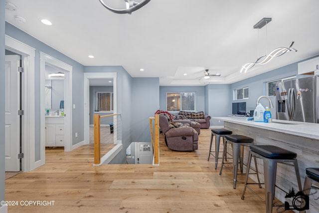 living room featuring a raised ceiling, ceiling fan, light hardwood / wood-style flooring, and sink