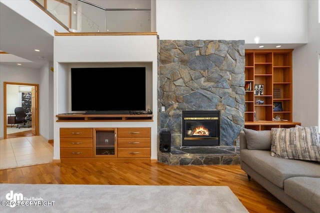 unfurnished living room with a towering ceiling, light hardwood / wood-style floors, and a stone fireplace