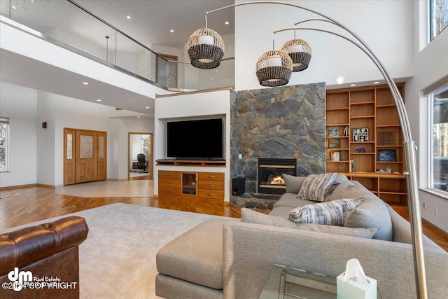 living room featuring a towering ceiling, light wood-type flooring, and a stone fireplace