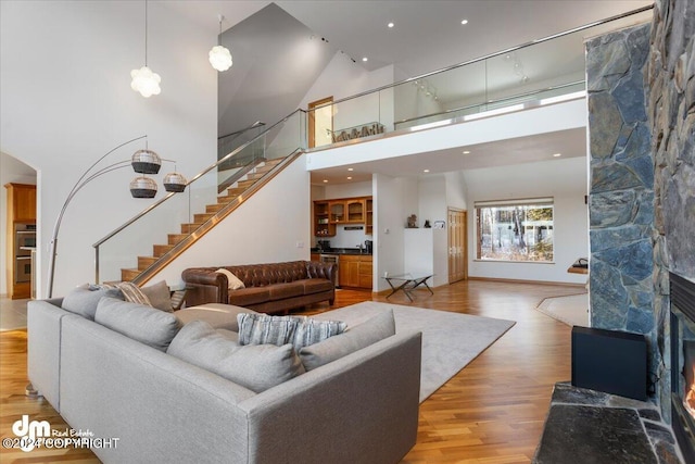 living room featuring a stone fireplace, light hardwood / wood-style flooring, and high vaulted ceiling