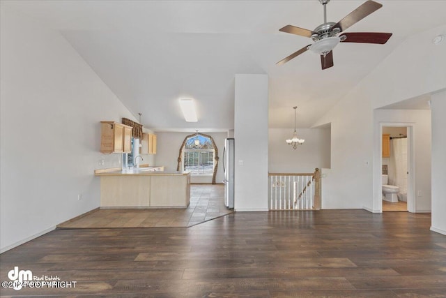 unfurnished living room with sink, high vaulted ceiling, dark wood-type flooring, and ceiling fan with notable chandelier