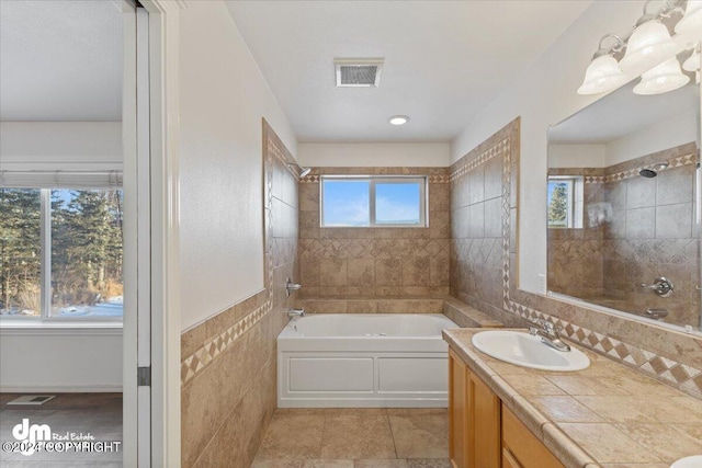 bathroom with tile patterned flooring, vanity, tiled shower / bath, and tile walls