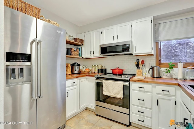 kitchen with appliances with stainless steel finishes, light tile patterned floors, butcher block countertops, and white cabinetry