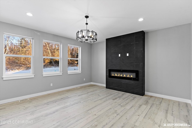 unfurnished living room featuring a tile fireplace, light wood-type flooring, an inviting chandelier, and plenty of natural light