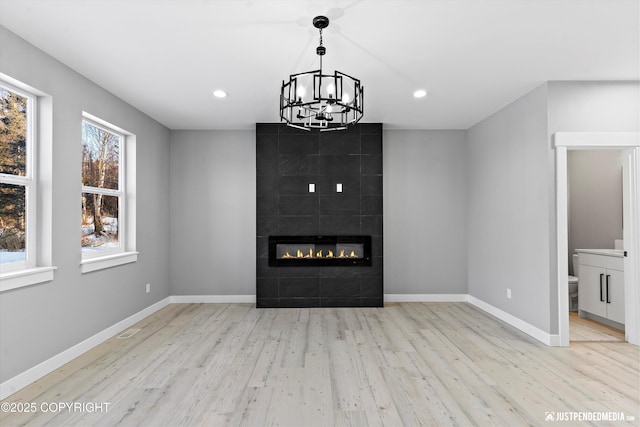 unfurnished living room featuring a notable chandelier, light hardwood / wood-style floors, and a tile fireplace