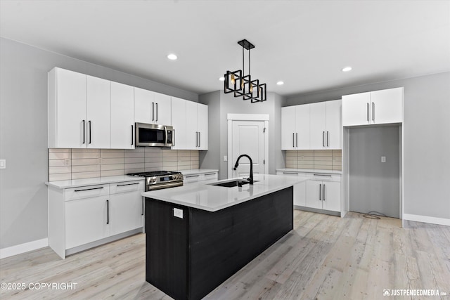 kitchen with sink, hanging light fixtures, a center island with sink, white cabinets, and appliances with stainless steel finishes