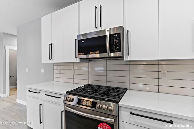 kitchen with light wood-type flooring, appliances with stainless steel finishes, backsplash, and white cabinetry