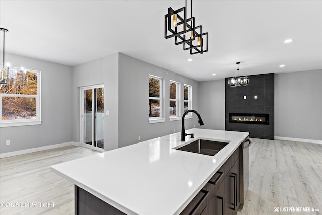 kitchen with pendant lighting, sink, light hardwood / wood-style flooring, an island with sink, and a tiled fireplace