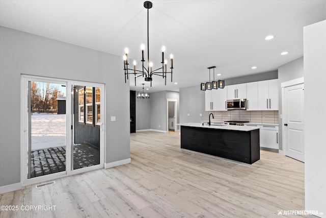 kitchen with pendant lighting, a kitchen island with sink, light wood-type flooring, tasteful backsplash, and white cabinetry