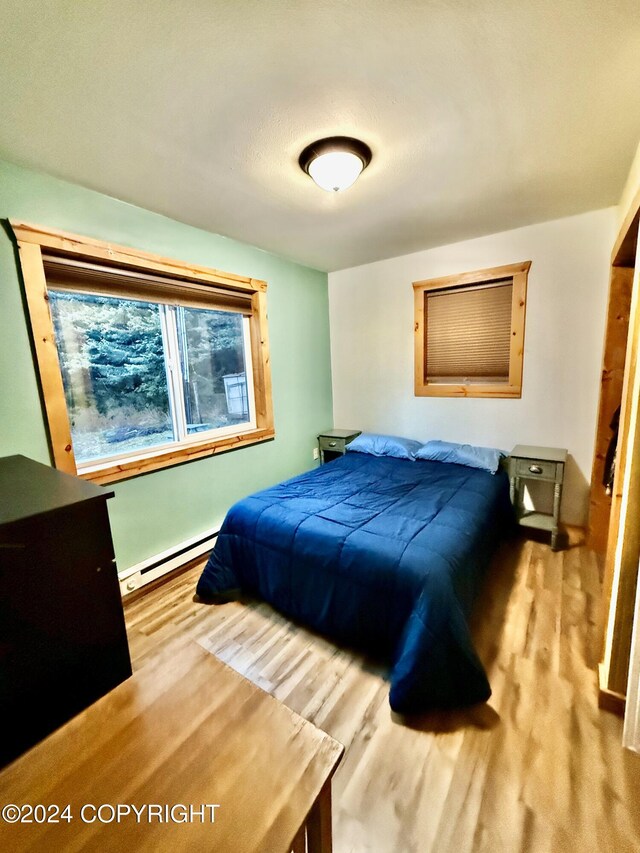 bedroom with light hardwood / wood-style floors and baseboard heating