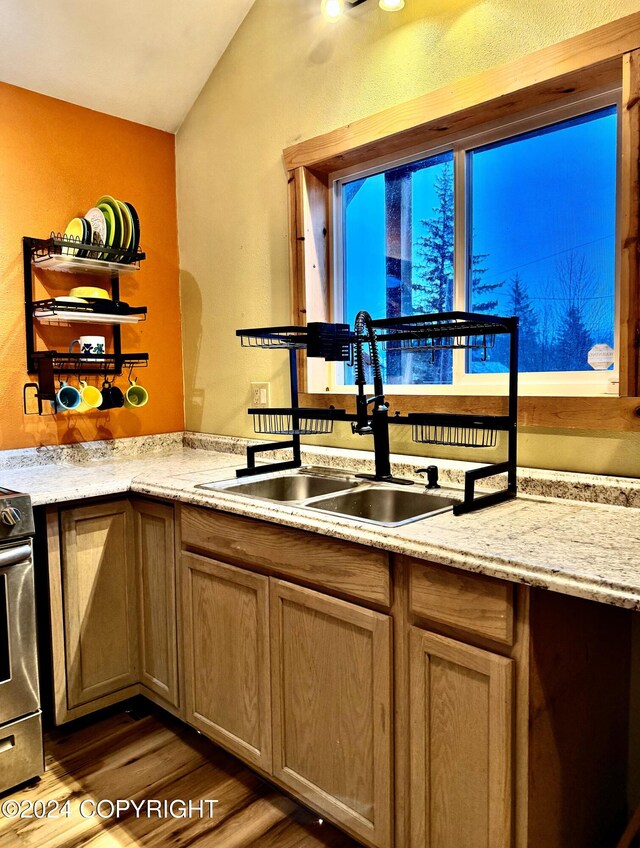 kitchen with light brown cabinets, sink, light stone countertops, stainless steel range, and wood-type flooring