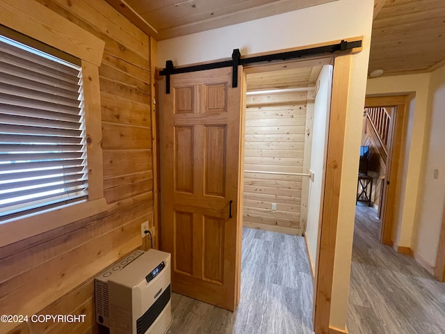 corridor with heating unit, wood walls, a barn door, and hardwood / wood-style flooring