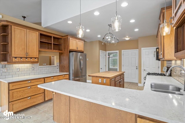 kitchen featuring pendant lighting, sink, tasteful backsplash, kitchen peninsula, and stainless steel refrigerator