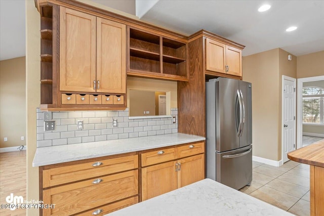 kitchen with stainless steel fridge, light stone counters, backsplash, and light tile patterned flooring