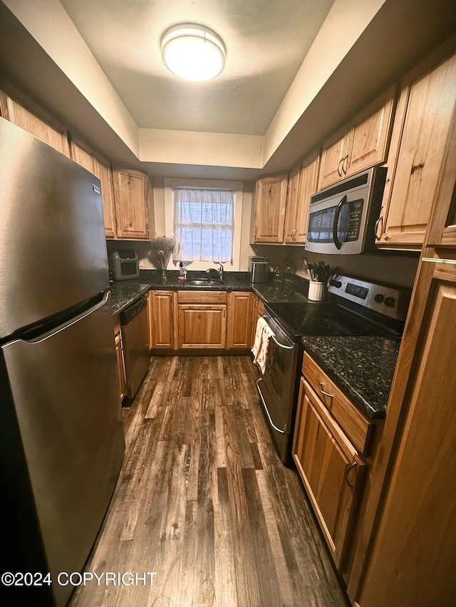 kitchen featuring sink, a raised ceiling, dark hardwood / wood-style flooring, dark stone counters, and appliances with stainless steel finishes