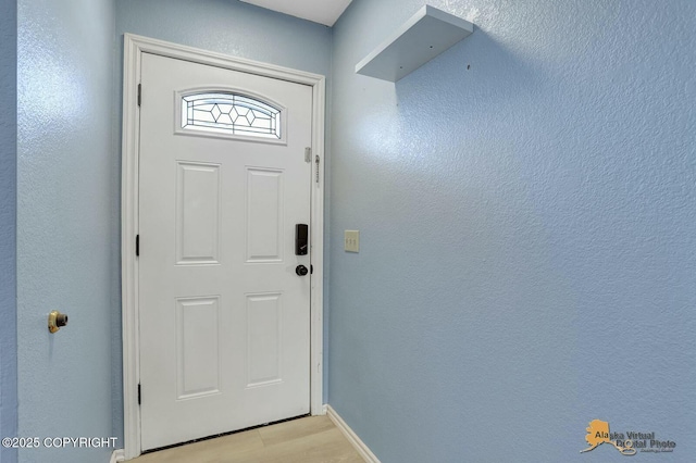 doorway to outside featuring light wood finished floors, baseboards, and a textured wall