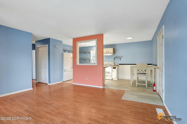 unfurnished living room with a sink, baseboards, and light wood-style flooring