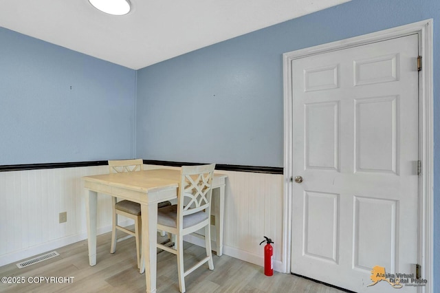 dining room featuring visible vents, light wood-style floors, and a wainscoted wall