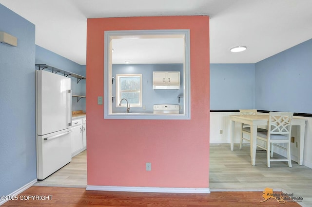 kitchen with white cabinets, light wood finished floors, range, and freestanding refrigerator