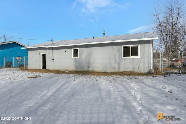 snow covered back of property with a gate, fence, and metal roof