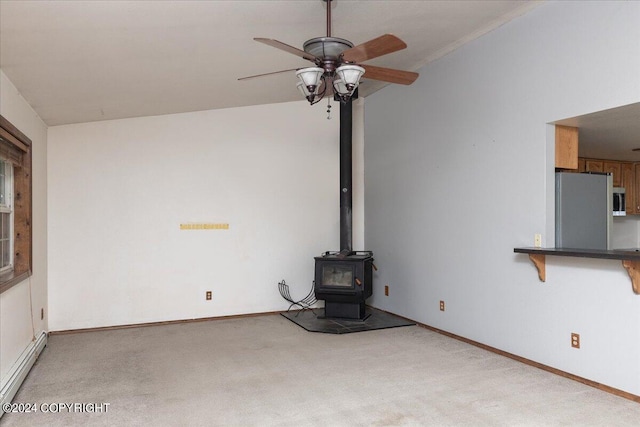 unfurnished living room with a wood stove, ceiling fan, light carpet, and a baseboard heating unit